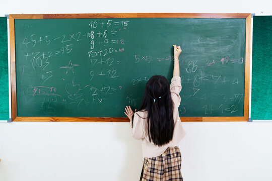 Young Asian girl solving math problem on blackboard