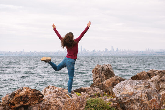Joyful traveler woman celebrates on rocky seaside