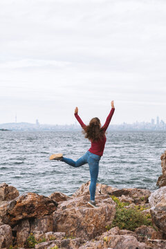 Joyful traveler woman celebrates on rocky seaside