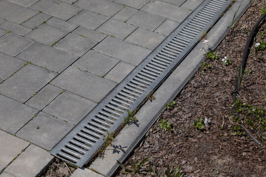 Concrete drainage channel with metal grate in paved yard. Shows effective urban stormwater drainage