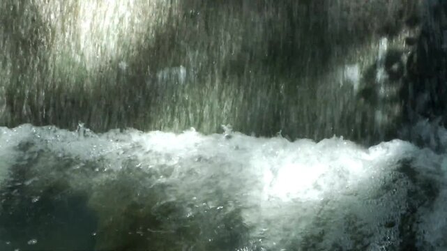 The waterfall flows rapidly over the rocks, creating ripples and alternating waves, a calming natural rhythm.