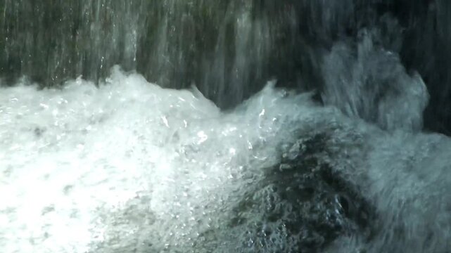 The waterfall flows rapidly over the rocks, creating ripples and alternating waves, a calming natural rhythm.