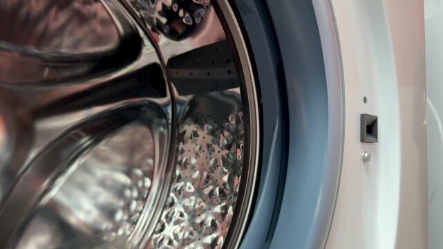 Close-up steel drum washing machine door showing gleaming stainless interior with perforated pattern, open rubber gasket, visible