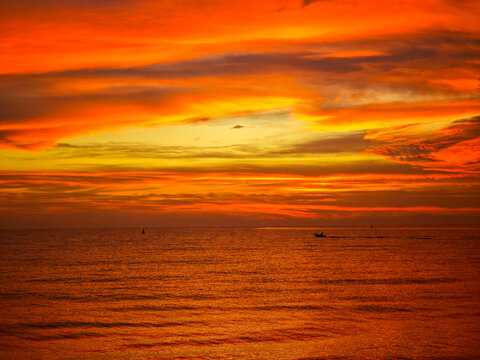 Dramatic Fiery Sunset Over Calm Ocean with Silhouetted Boat, Vibrant Orange Red Sky Reflecting on Sea Water, Golden Hour Seascape