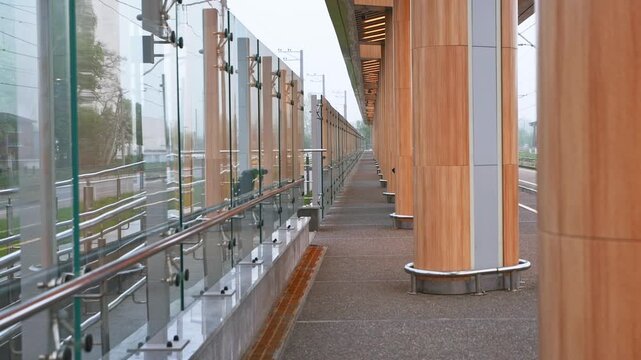 Modern railway station platform with glass panels and wooden pillars in overcast light