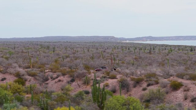 Aerial view shows SUV towing teardrop camper trailer away from campsite on Mulege beach next to the Sea of Cortez and desert.