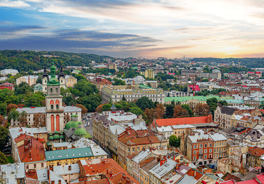 Panoramic view of the historic old town of Lviv, Ukraine, featuring colorful building rooftops and church towers under a sunset sky.