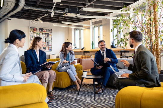 Business team collaborating in modern office lounge, diverse professionals discussing corporate strategy during informal meeting