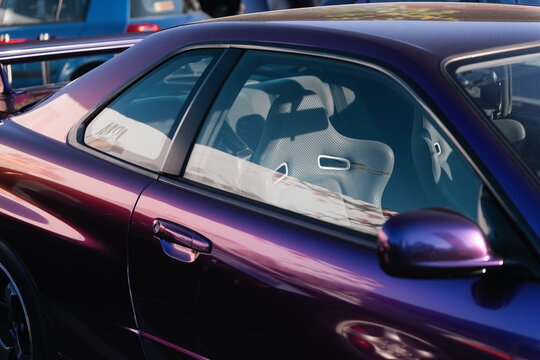 Close-up side view of midnight purple Nissan Skyline R34 GT-R coupe in parking lot, highlighting the sports bucket seat in bright sunlight seen through the window glass. Kyiv, Ukraine - May 16 2026