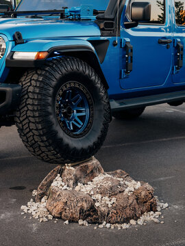 Low-angle view of a lifted eep Wrangler crawling a rock, highlighting suspension articulation. Blue SUV with off-road tires and lots of overlanding accessories. Kyiv, Ukraine - May 16 2026