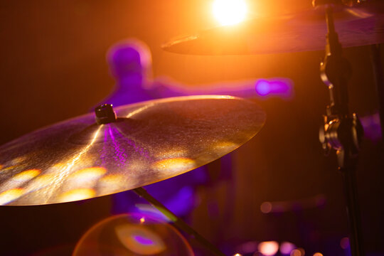 Close-up of drum kit cymbals on stage during a live music concert with a blurred drummer in the background