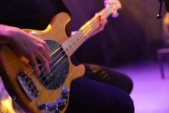 Close-up of a musician hand playing a five-string electric bass guitar during a live concert on stage