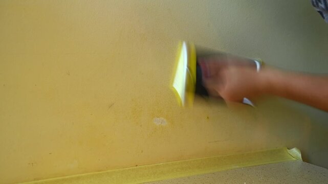 Hand sanding painted wall patch near countertop in interior
