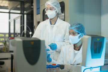 Naklejka premium Two female researchers in white lab coats, masks, and gloves collaborate over scientific instruments, ideal for healthcare, biotech, and pharmaceutical