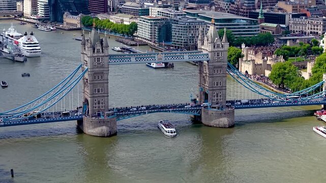 Establishing aerial view of the Tower Bridge area in London during a sunny summer day with river boat traffic and tourist crowds
