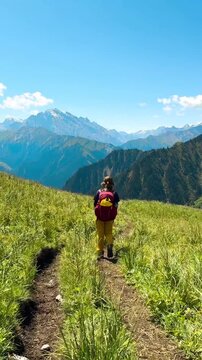 Wide-angle view of green grassy hills on both sides at Tianshan Mountain, Xinjiang, China. A woman walking in the distance on a sunny day. Many mountains are forming beautiful layers.