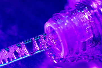 Close-up of a glass dropper releasing clear liquid with bubbles. Purple lighting, soft focus, and molecular texture evoke biotech beauty and futuristic skincare innovation. © Katerina