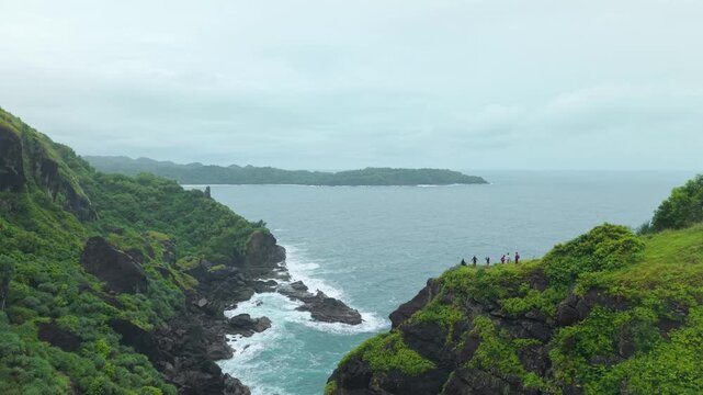 Aerial view of Bukit Pengilon coastal cliffs with people standing on the edge overlooking the ocean in Kecamatan Tepus, Yogyakarta, Indonesia.