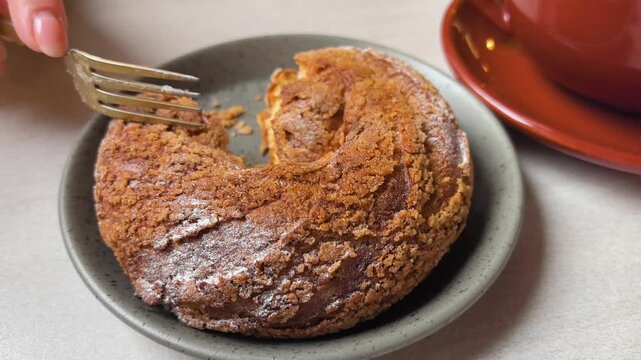 Enjoy the delightful moment of indulging in a warm pastry, revealing its creamy filling. Sipping coffee compliments the sweetness as hands share in the treat's enjoyment.