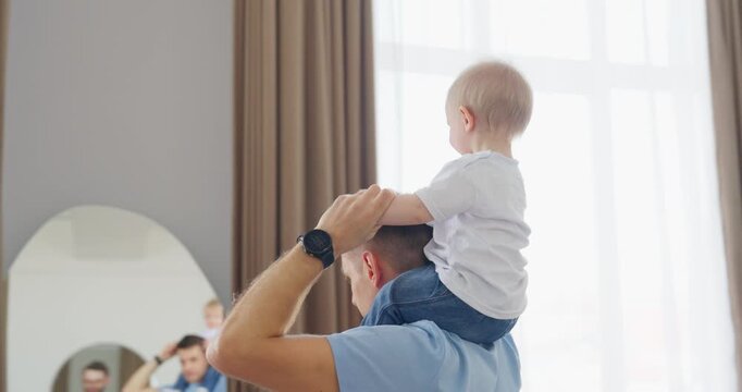Happy father carrying his toddler on his shoulders in a bright home, sharing playful bonding moments and gentle family affection indoors
