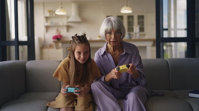 Happy girl and her grandma playing video game with controllers, family pastime