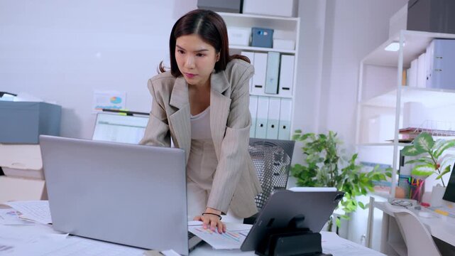 Serious business woman standing by modern corporate office desk working on important project looking at laptop screen showing stressed focused expression during demanding workday having problem