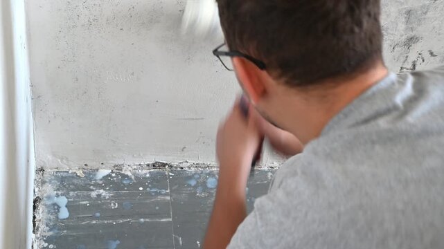 Man priming interior plaster wall with roller in renovation room