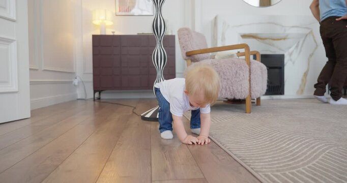 Blond toddler learning to crawl and walk across a cozy modern living room while parents watch and encourage first steps at home