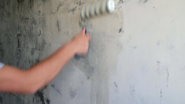 Person rolling primer over concrete wall during interior renovation