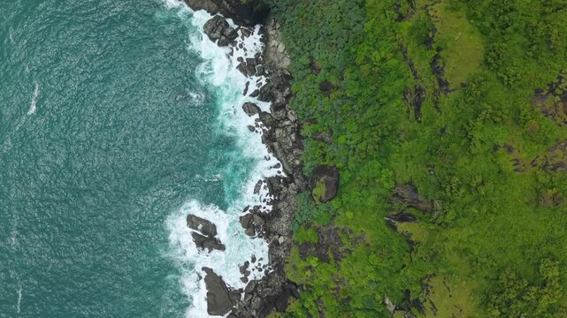 Aerial view of Bukit Pengilon with turquoise waves crashing against dark rocks and lush green vegetation Kecamatan Tepus, Daerah Istimewa Yogya, Indonesia.