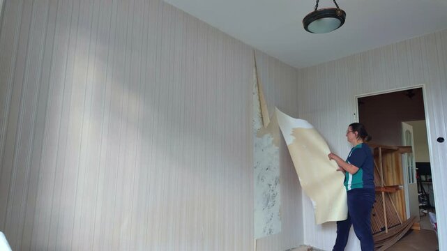 Woman stripping wallpaper from interior room wall during renovation  in timelapse