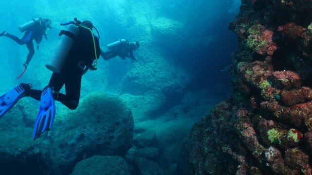  scuba divers exploring   reefs walls and caverns  underwater deep blue water big rocks and bubbles ocean scenery 