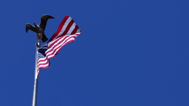 American flag waving in breeze with eagle statue against blue background in Fairmont, West Virginia