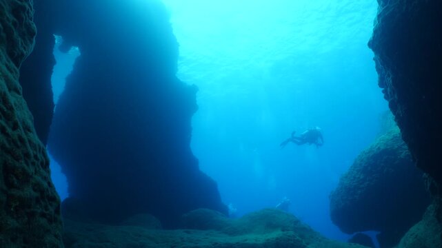  scuba divers exploring   reefs walls and caverns  underwater deep blue water big rocks and bubbles ocean scenery 