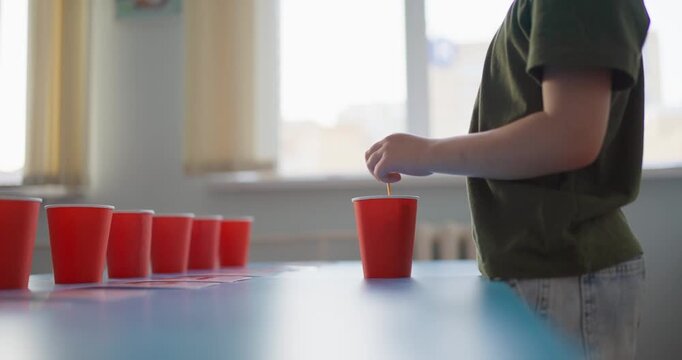 Young boy concentrating while arranging red plastic cups in a bright classroom, practicing a playful coordination and memory activity at a table