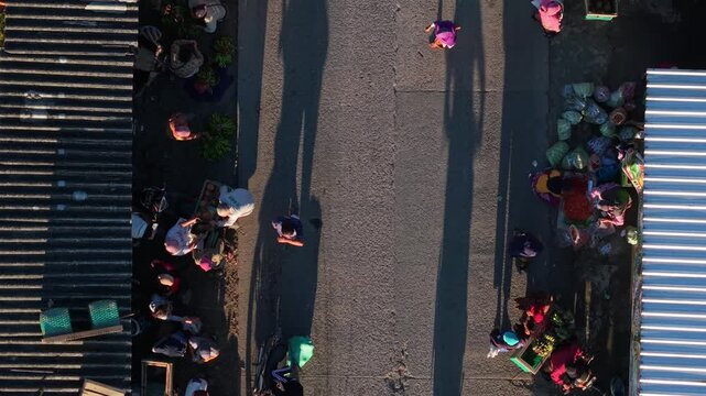 Aerial view of people gathered at a local street market with a motorcycle passing by and long shadows on the road in Kemalang, Central Java, Indonesia.