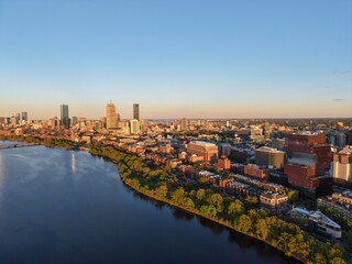 Fototapeta premium Golden hour aerial drone view of the Boston skyline, featuring the Prudential and John Hancock towers rising above the historic Back Bay neighborhood and the calm waters of the Charles River