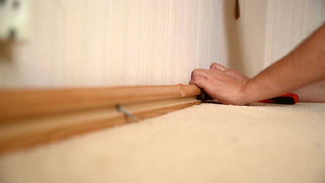 Man removing wooden baseboard molding along interior wall on carpet