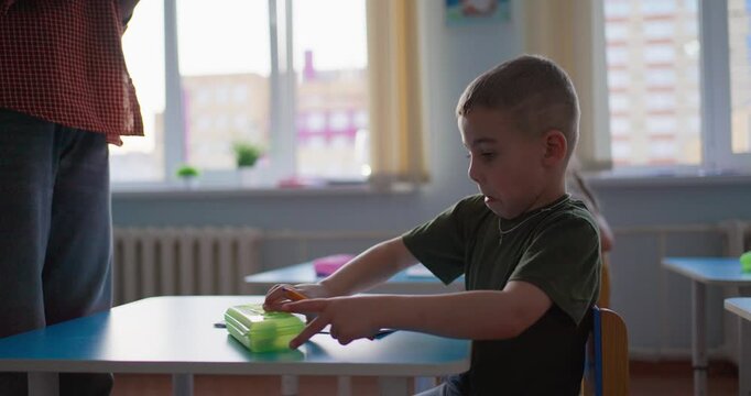 Young students sitting at classroom desks with notebooks and pencils while a teacher explains a lesson near bright windows in a calm learning environment