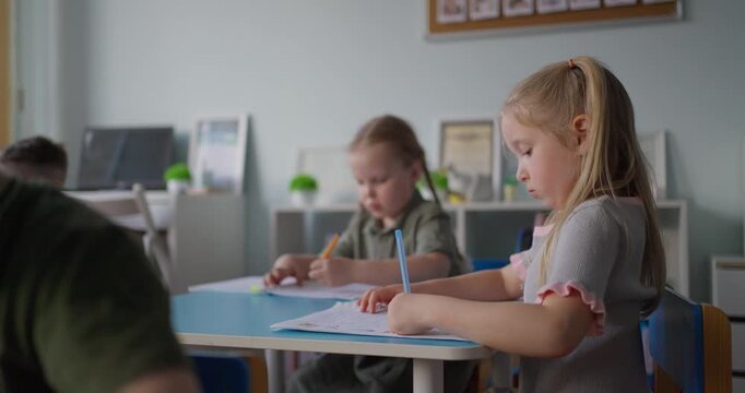 Young schoolchildren sit at classroom desks writing in notebooks with pencils during a quiet lesson, focused on learning and early education