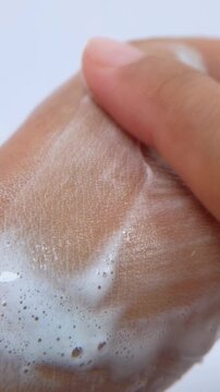 Rubbing soap slowly on the back of hand. Close up view isolated on white background. Skin covered with soap foam.
