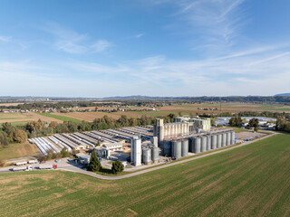 This aerial view shows an industrial facility surrounded by fields and trees, with silos and roads visible in the landscape. © 24K-Production