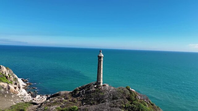 Aerial approach toward Ke Ga Lighthouse standing on a rocky island surrounded by the South China Sea near Phan Thiet, Binh Thuan, Vietnam.