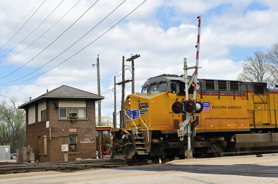 A Union Pacific locomotive, leading a freight train, approaches a diamond crossing beneath a still operating control tower. The diamond is also adjacent to a grade crossing.
