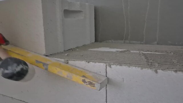 Building an aerated concrete block wall, front view, worker adjusting with a rubber mallet and checking with a spirit level.