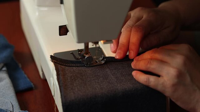 Woman sewing denim fabric close up on sewing machine. Focus on hands and process. Concept of DIY , handmade work 