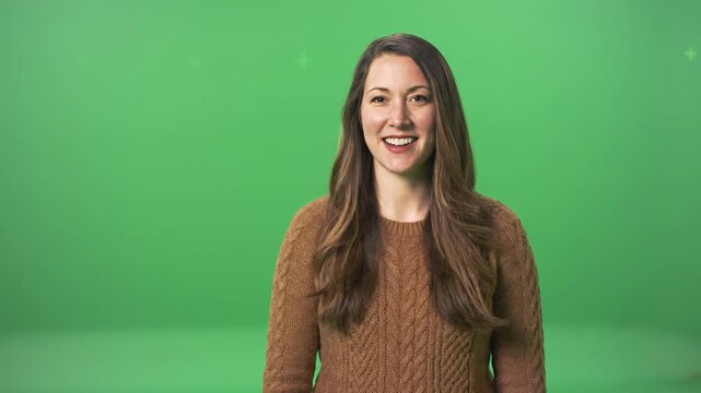 A young caucasian woman with long chestnut-brown hair wearing a brown knitted sweater smiles engagingly against a pristine chroma key green background, studio lit. Professional commercial portrait