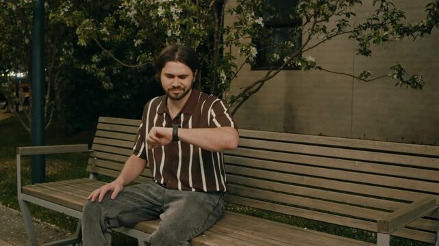 Couple sits on bench in park while man gestures angrily after long wait. Tense date scene shows disappointment and conflict.