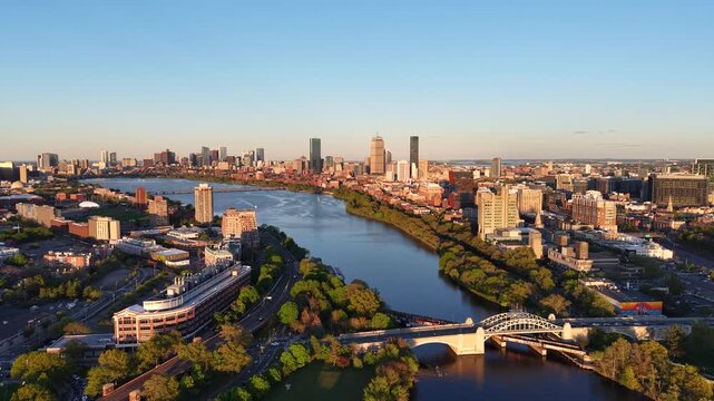 Golden hour aerial drone view of the Boston skyline, featuring the Prudential and John Hancock towers rising above the historic Back Bay neighborhood and the calm waters of the Charles River.