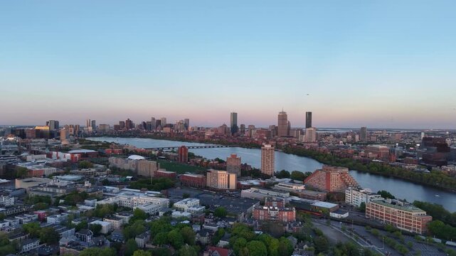 Golden hour aerial drone view of the Boston skyline, featuring the Prudential and John Hancock towers rising above the historic Back Bay neighborhood and the calm waters of the Charles River.
